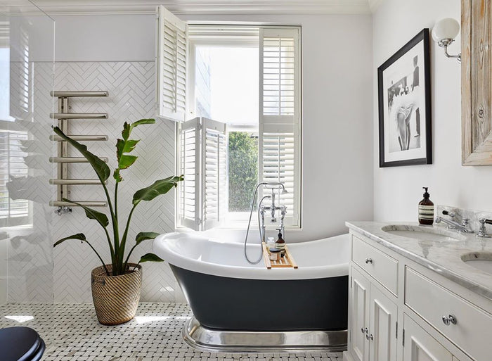 white bathroom with free standing bath tub and window with tier on tier half open shutters