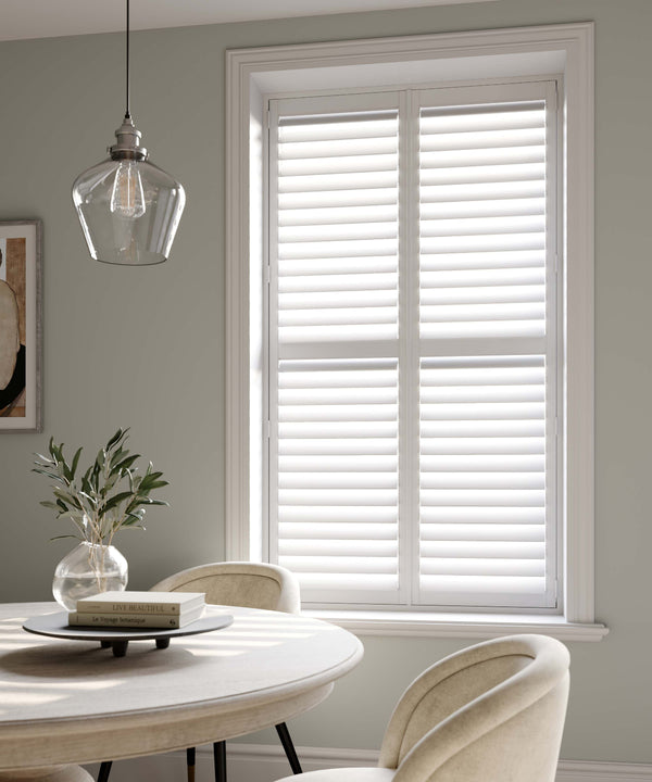 Dining room with white shutters on a window, round table, and chairs.