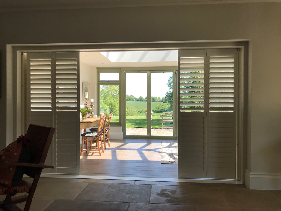 Sliding shutter panels opened along a track across a wide glazed room opening