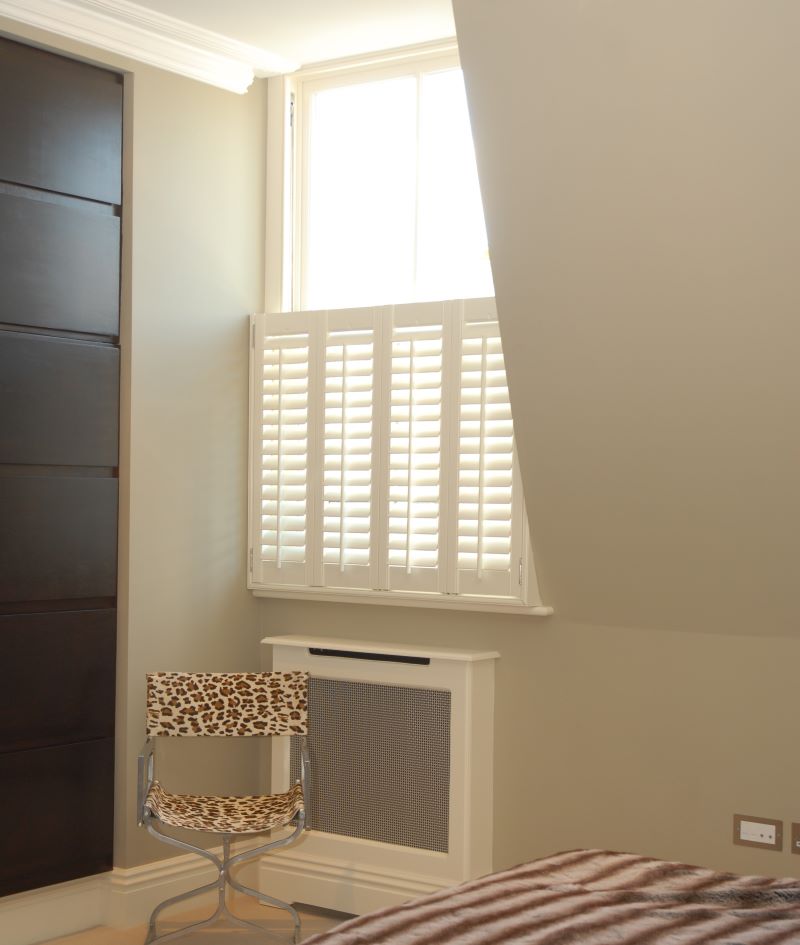 corner of a bedroom with light coming through a small window with cafe shutters