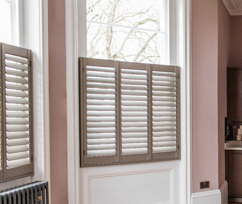 Window with wooden shutters in a room with pink walls and a radiator.
